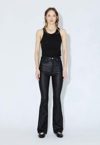 Černý top bez rukávů doplněný vysokými koženými kalhotami s rozšířenými nohavicemi. Jednoduchý design s minimálním množstvím kovových doplňků a hladkou texturou.