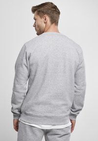 Sudadera gris con cuello redondo, mangas largas y puños acanalados. Textura suave y dobladillo redondeado, que muestra un diseño minimalista.