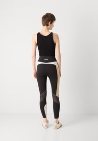 Top sportivo nero abbinato a leggings aderenti con dettagli neri, beige e in rete, e una fascia larga con il marchio "BOSS".