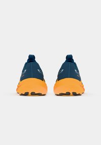 Blauwe sportschoenen met een oranje zool, voorzien van een gestructureerd bovenmateriaal, een trekband aan de hak en zwarte grippatronen op de zool.