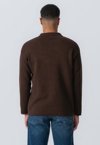 Brun langærmet strikket pullover med en afslappet pasform og krave, parret med blå denim jeans. Stoffet har en glat tekstur.