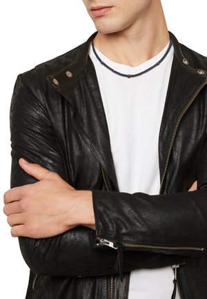 Black leather biker jacket with silver zippers, snap collar, and subtle texture. White t-shirt underneath, worn with a beaded necklace.