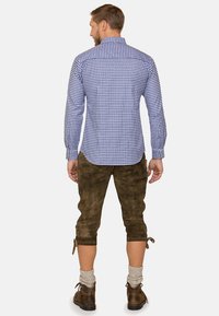 Blau-weiß kariertes Langarmhemd kombiniert mit braunen Wildleder-Lederhosen, die seitliche Schnürungen und eine knielange Ausführung haben. Braune Schuhe inklusive.