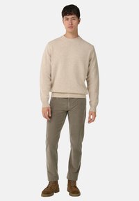 Bēša adīta džemperis ar apaļu kaklu, ribotām piedurknēm un apakšmalu, kombinēts ar olīvzaļiem korduroja biksēm un brūniem zābakiem ar auklām.