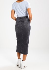 Falda midi de denim negro con un diseño ajustado, talle alto, costuras sutiles y bolsillos traseros. Combinada con una camisa azul clara y botines blancos.