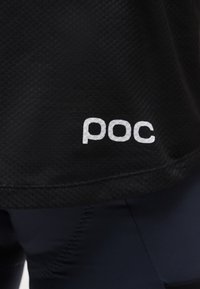 Κοντινό πλάνο σε μαύρο υφασμάτινο ύφασμα με λευκό λογότυπο "poc" τυπωμένο κοντά στην κάτω άκρη ενός ενδύματος.