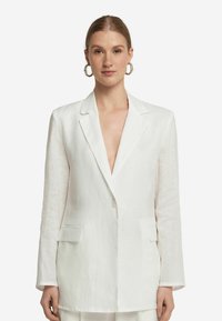 Vit linneblazer med skarp slag, enknapplåsning, två framfickor och långa ärmar, med en avslappnad passform och minimal textur.