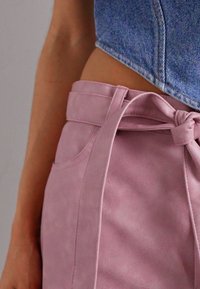 Fialové nohavice z umelé kože s vysokým pásom a viazacím pásom, hladká textura, bočné vrecká a bezšvové šitie. Časť denimu hornej časti je viditeľná.