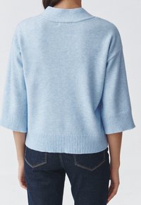 Pull tricoté bleu clair avec col, manches 3/4, poignets et ourlet côtelés. Caractérisé par une texture douce et un design minimaliste.