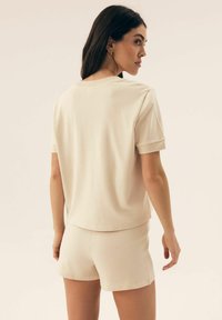 Krótki rękaw, jasnobeżowa bluzka i dopasowane szorty o subtelnej prążkowanej teksturze. Prosty krój z luźnym fasonem, bez wyraźnych elementów dekoracyjnych.