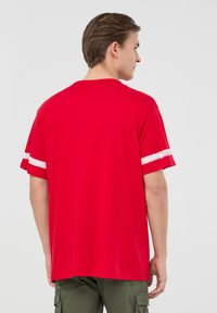 T-shirt in cotone rosso con collo rotondo, maniche corte e strisce bianche sulle maniche; texture liscia, vestibilità regolare.