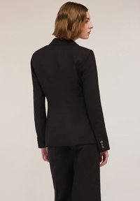 Czarny żakiet o dopasowanej sylwetce, z zapięciem na jeden guzik i skrojonym kroju. Posiada gładką teksturę tkaniny oraz subtelne poduszki na ramionach.