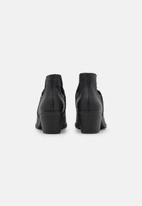 Botas de tobillo de cuero negro con una superficie texturizada y un tacón afilado. Cuenta con paneles laterales elásticos para facilitar su uso.