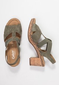 Olivgrön nubucksandaler med en korkblockklack, med korsade remmar och en flätad detalj runt sulan.