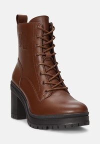 Bruine leren enkellaarzen met een hoge blokhak, ronde neus en een vetersluiting aan de voorkant. Voorzien van een gestructureerde zool en een gegraveerd logo.