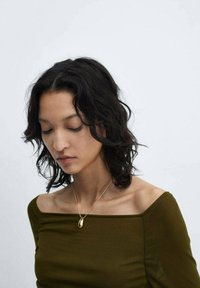 Zlate kapljaste viseče uhan na vitki verigi, nosijo se preko olivno zelene majice brez naramnic, kar poudarja ton in teksturo kože.