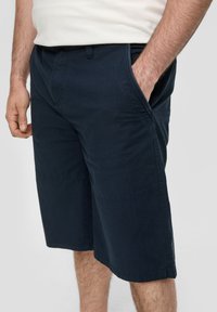 Shorts en coton bleu marine avec une coupe décontractée, dotés de poches latérales, d'une texture lisse et de détails de couture visibles.