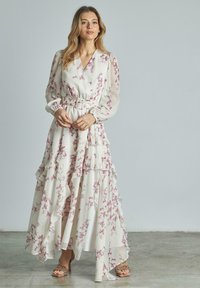 Abito maxi bianco a fiori con maniche lunghe, scollatura a V, strati arruffati e vita cinturata decorata con motivi floreali rosa.