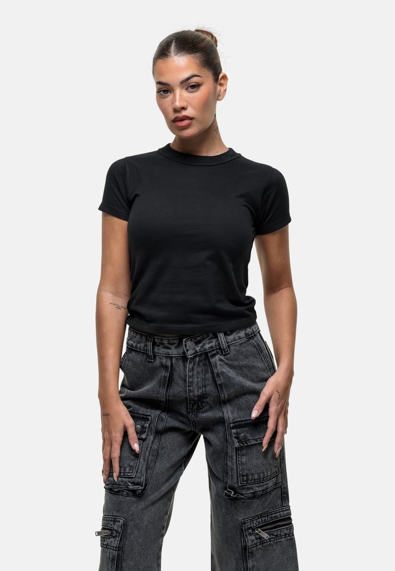 T-shirt noir à manches courtes en coton, associé à un pantalon cargo gris avec de multiples poches et zippers, présenté sur un fond uni.