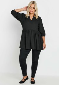 Top peplum nero con scollo a V e maniche 3/4, realizzato in un tessuto testurizzato. Abbinato a pantaloni neri aderenti e scarpe basse nere.