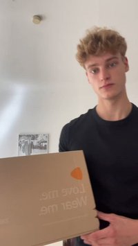 Pruun pappkast, mille peal on valge tekst "Armasta mind. Kanna mind." ning eristuv oranž logo. Kast on käes inimesel, kes kannab musta särki.