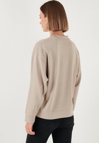Felpa beige con una vestibilità rilassata, maniche lunghe e polsini a coste. Texture morbida, design casual con scollatura a girocollo e cuciture minime.