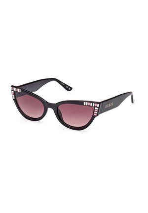 Gafas de sol negras de estilo cat-eye con lentes degradados en rosa y acentos rectangulares decorados con joyas en la montura. Nombre de la marca "GUESS" exhibido en el lateral.