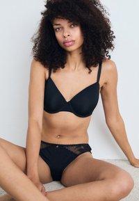 Reggiseno nero senza cuciture con spalline regolabili, abbinato a perizoma nero con bordo in pizzo che presenta un accento decorativo in vita.