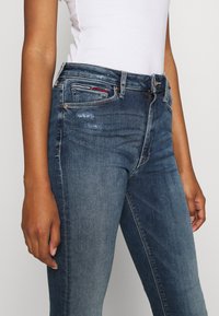 Tmavě modré denimové džíny se slim fit, s minimálními oděrkami, středně vysokým pasem, pěti kapsami a zapínáním na zip.