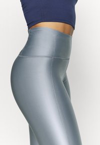 Legginsy fitness z wysokim stanem w gładkim, jasnoniebieskim materiale o delikatnym połysku. Posiadają wzmocnione szwy wzdłuż szwów.