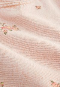 Tejido de color rosa claro con una sutil textura de rayas diagonales, con pequeñas bordaduras florales en tonos rosa y verde.