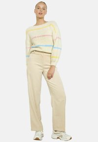 Pull en tricot blanc cassé avec des rayures pastel ; poignets côtelés. Pantalons en velours côtelé beige. Le modèle porte des baskets blanches avec des accents beiges.