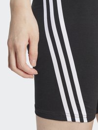 Shorts atletici negri, cu o croială strânsă, având trei dungi verticale albe pe laterale și o textură de țesătură moale și elastică.