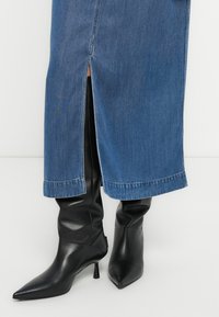 Σκούρα μπλε τζιν φούστα με πλαϊνή σκίσιμο, συνδυασμένη με μαύρα δερμάτινα μποτάκια αστραγάλου με μυτερή μύτη και ψηλό τακούνι στιλέτο.