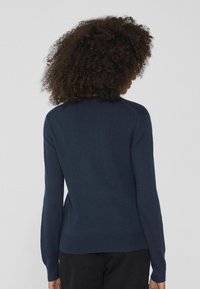 Marineblauer Strickpullover mit langen Ärmeln, rundem Ausschnitt und geripptem Saum. Glatte Textur mit dezenten Nähdetails.