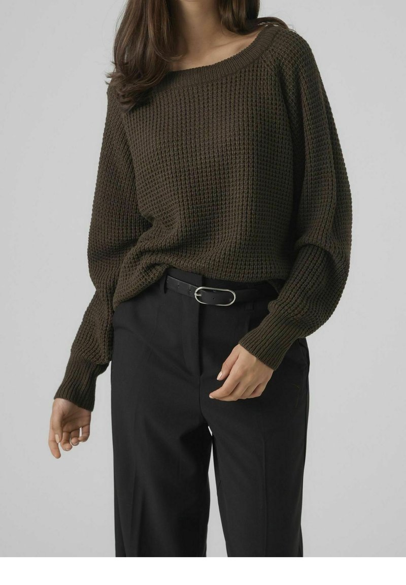 Maglione marrone lavorato a maglia con vestibilità ampia e scollatura larga, abbinato a pantaloni neri a vita alta, accentuati da una cintura sottile.