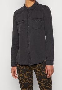 Donkergrijze denim overhemd met lange mouwen, knoopsluiting aan de voorkant, twee borstzakken en een ronde zoom. Heeft contraststiksels en een klassieke kraag.