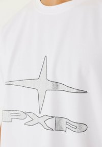 Witte katoenen t-shirt met een zwart en zilveren strass sterrenontwerp en de tekst "PXR" op de voorkant. Ronde hals en korte mouwen.