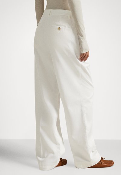 Vide hvite bukser i mykt stoff, med en baklomme med knappedetalj. Kombinert med brune loafers og en lys topp.