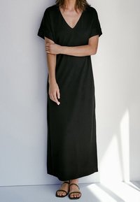 Musta maxi-mekko, jossa on lyhyet käännetyt hihat ja V-pääntie. Valmistettu sileästä kankaasta, siinä on suora siluetti ja se ulottuu nilkkoihin.