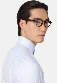 Kulaté želvovinové brýle s průhlednými skly; světle modrá košile s kostkovaným vzorem a širokým límcem; hladký povrch látky.