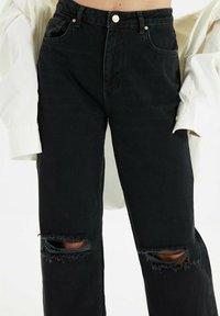 Jeans in denim nero a vita alta presentano un design a gamba dritta, aperture strappate sulle ginocchia e un classico stile a cinque tasche.