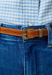 Cinturón de cuero marrón con una hebilla de plata ornamentada, usado sobre una camisa de cuadros azules y jeans de denim azul.