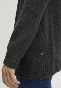 Mörkgrå stickad cardigan med en texturerad yta, med ribbade mudd och nederkant samt en svart knapppdetail på sidan.