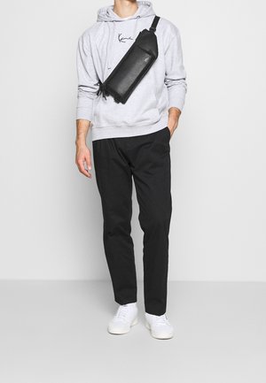 Borsa a tracolla in pelle nera indossata sopra una felpa grigia, abbinata a pantaloni neri e scarpe da ginnastica bianche. Presenta un design elegante e minimalista.