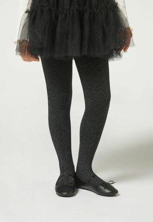 Collant neri con una texture scintillante, abbinati a ballerine nere con dettagli a fiocco; indossati sotto una gonna di tulle nera.