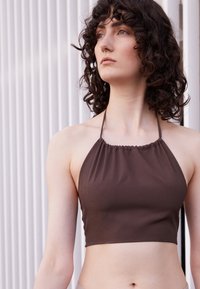 Top halter castanho com decote franzido, feito de um tecido liso, apresentando um design cropped que se estende logo acima da cintura.