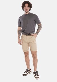 Maglietta grigia a maniche corte, pantaloni beige e sneaker marroni e bianchi. I pantaloni hanno i risvolti e la maglietta presenta una texture liscia.