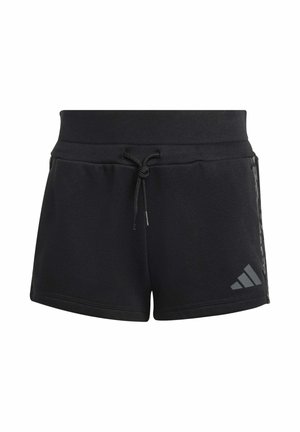 Niña vistiendo ropa deportiva negra de Adidas, pantalones cortos negros, calcetines a rayas y zapatillas, sosteniendo una chaqueta sobre el hombro y sonriendo.