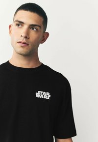Tricou din bumbac negru, cu un logo alb "Star Wars" în zona stângă a pieptului. Guler rotund și mâneci scurte. Textură netedă.